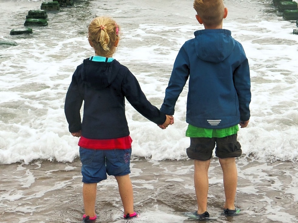 Zwei Kinder gehen Hand in Hand am Meer entlang